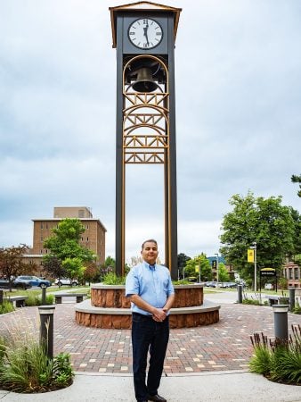 A Michigan Tech leader stands in front of the clock tower on campus outside in summer.