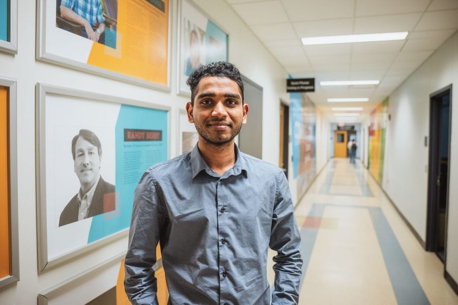 A Michigan Tech Computer Science PhD student smiles for a portrait with the College of Computing's Rekhi Hall in the background.