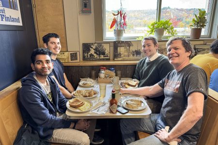 Four people at a booth in a restaurant smile with full plates of delicious breakfast before them after a tutoring sessions at Portage Lake District Library.