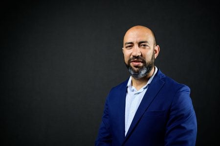 A Michigan Tech researcher in a blue suit against a dark portrait background.