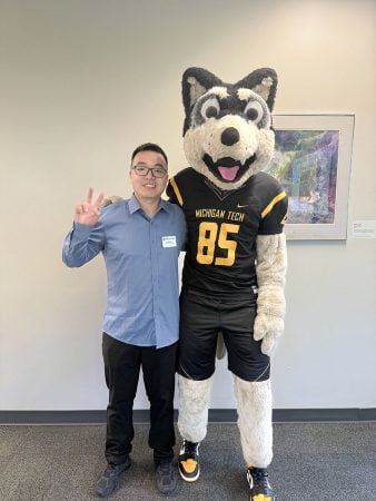 A Michigan Tech faculty member flips the peace sign as he poses with University mascot Blizzard T. Husky.