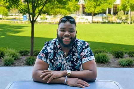 A Michigan Tech student sits at a table smiling outdoors on campus in the summer.