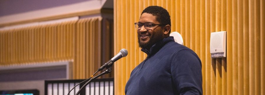 Christopher Sanders smiles and stands in front of a microphone.