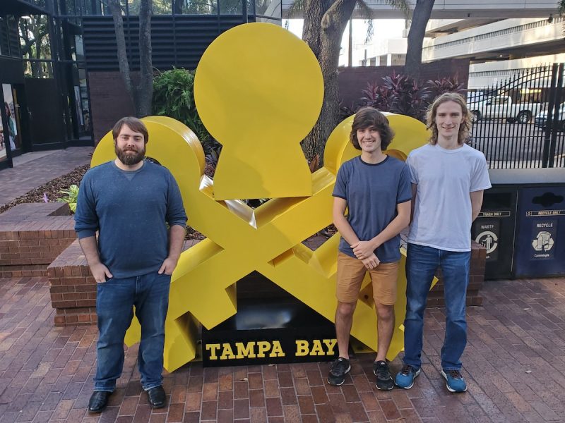 Three students standing near the Tampa Bay logo outside.