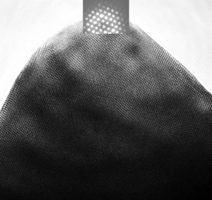Atomic resolution image of a spinel intergrowth lithium ion battery electrode particle and associated convergent beam electron diffraction pattern. The ordered dots all over the black triangle (the particle) are atomic columns, with a convergent beam electron diffraction pattern in white at the top. These results were obtained with the FEI 200kV Titan Themis Scanning Transmission Electron Microscope (S-TEM) recently commissioned by Michigan Tech.