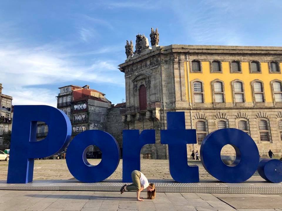 Amber does a yoga sign in front of a large blue lettered sign reading PORTO in Porto, Portugal