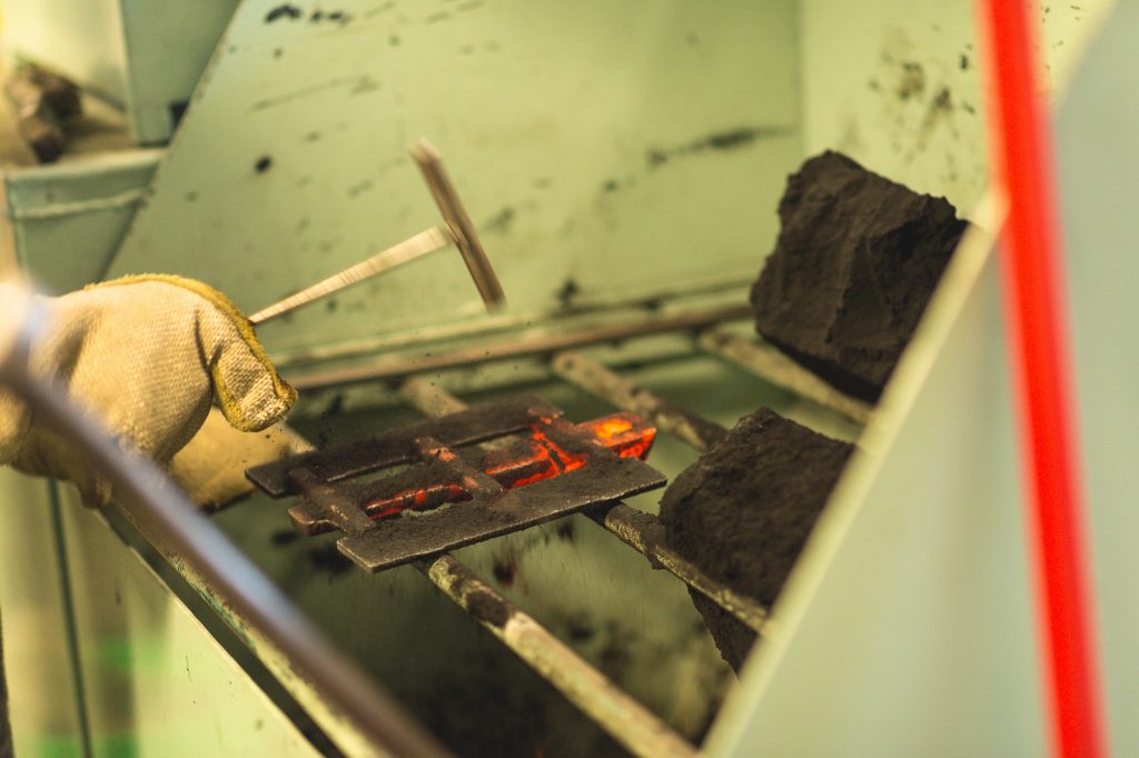 The molds are dumped into the shake-out bin where they disintegrate. Because sand is a good insulator the castings are still very hot after shake-out, as evidenced by the still glowing runner section. A few taps with a hammer loosens the sand. This green sand will be reused to make more molds after it is conditioned and remixed with water.