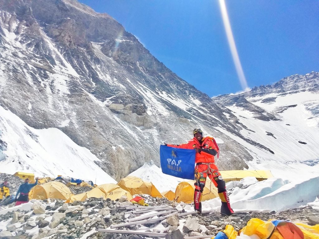 Seyoum at Camp 2 holding up a big blue flag that says Walia prior to heading up to Camp 3, and higher. Walia beer, a product of Heineken primarily sold in Ethiopia, was one of Seyoum's climbing sponsors.