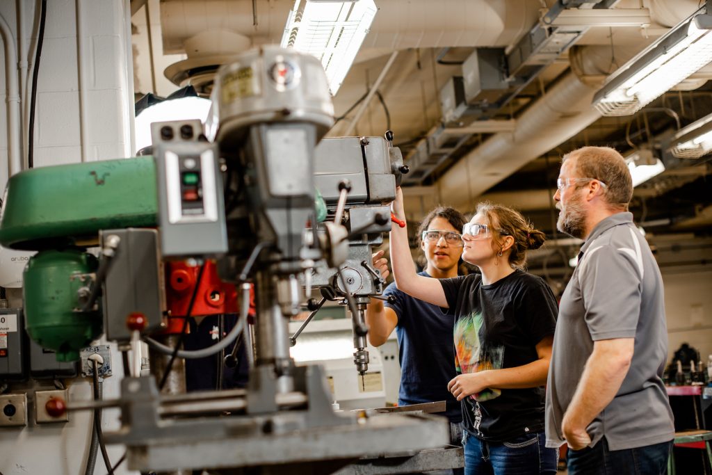 The Department of Manufacturing and Mechanical Engineering Technology maintains a machine shop with comprehensive facilities available to Michigan Tech students. The shop also offers machining and fabrication services for the university research community. Students and a faculty member examine a large drill in the machine shop.