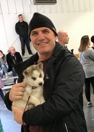 Coach Shawhan holds a tiny Husky pup in his arms.