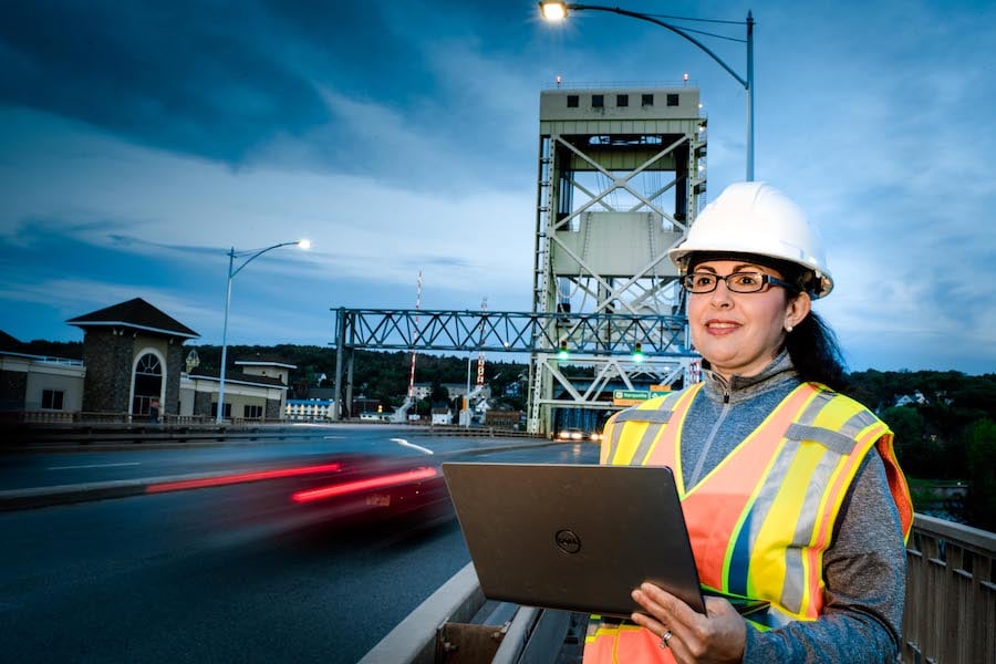 Aurenice Oliveira wearing gear and using a laptop on the Portage Lift Bridge.