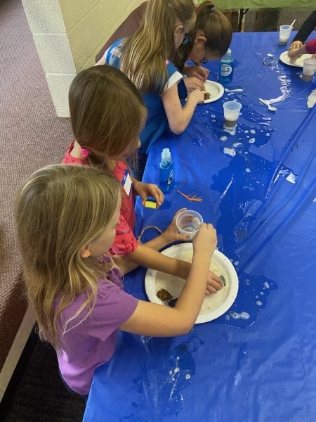 Girls work with soapy materials at a tabletop.