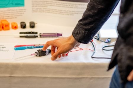 finger points at small student-designed device on a table