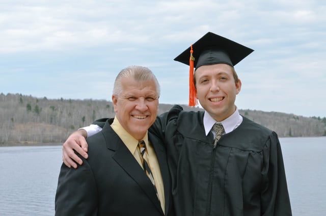 Zachary wears his cap and gown and has his arm around his father's shoulder.