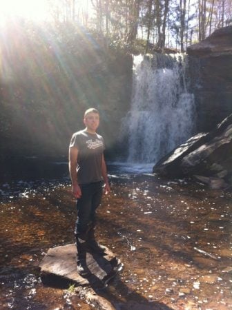 Zachary stands on a stone, in front of a roaring waterfall