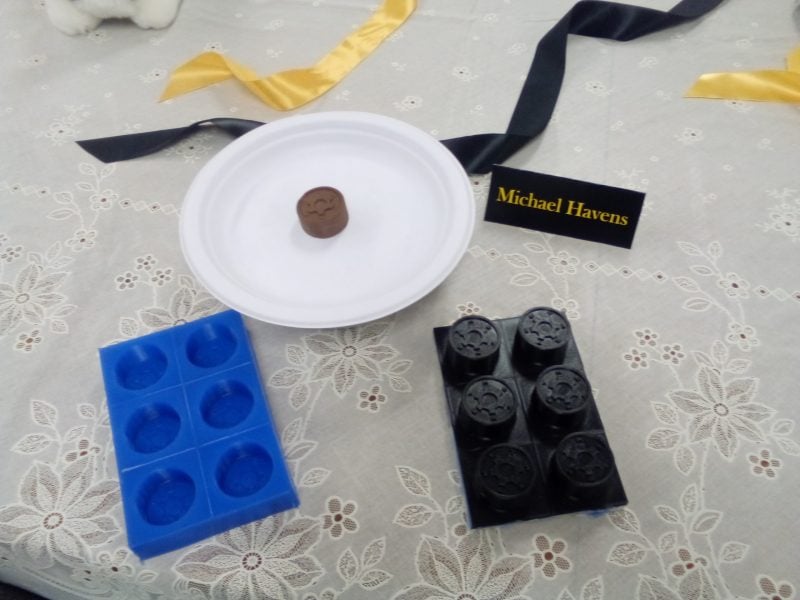 A plate with a single chocolate on a table, with the mold and 3d print.