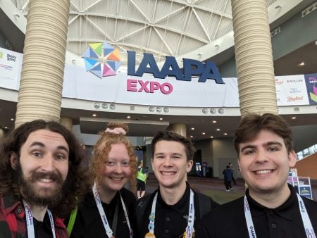 Four students stand in front of the IAAPA Expo sign at the entrance.