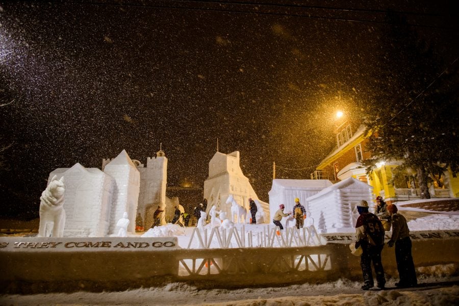 students work on large snow statues at night with snowflakes flying