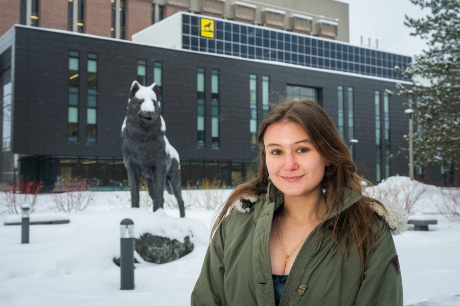 Aliyah Maxwell-Abrams in a winter coat standing in front of a snow covered Husky Statue.