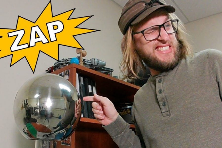 Shane Oberloier with a Van De Graaf generator and a yellow explosion graphic that says “ZAP!”