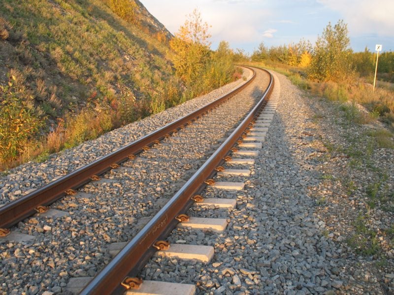 Railroad tracks curving around a green hill with shrubs on either side. 