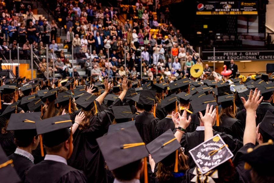 A crowd of Michigan Tech graduating students wearing their caps and gowns with the audience in the background.
