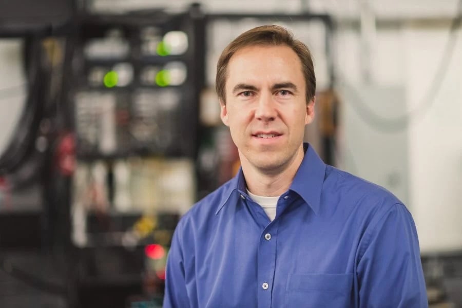Brad King poses in a blue button-up shirt in front of a tall server.