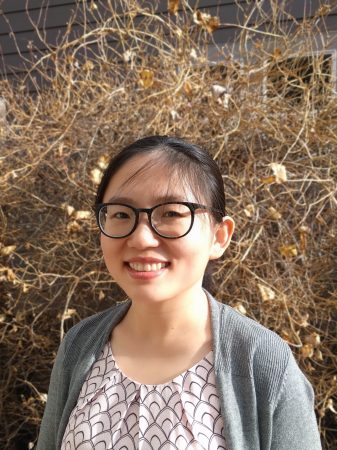 Yanrui (Daisy) Ning smiles in a portrait wearing a patterned white blouse, gray cardigan, and glasses.