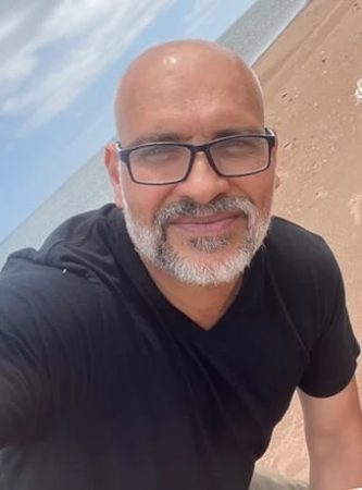  Behzad Akbari smiles in self-taken portrait on a beach, wearing a black polo and glasses