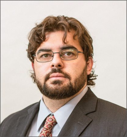 Andrew Oliva poses in a professional headshot wearing a charcoal suit, gray shirt, red patterned tie, and glasses.