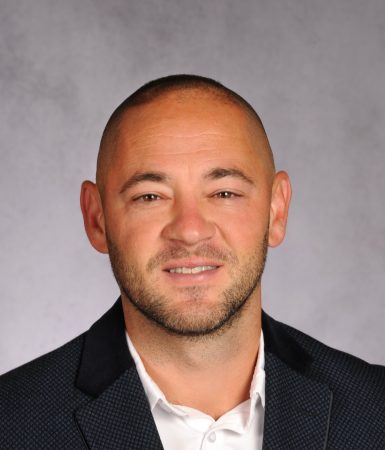 Caleb Stetson poses in a professional headshot wearing a blue patterned blazer and white shirt.