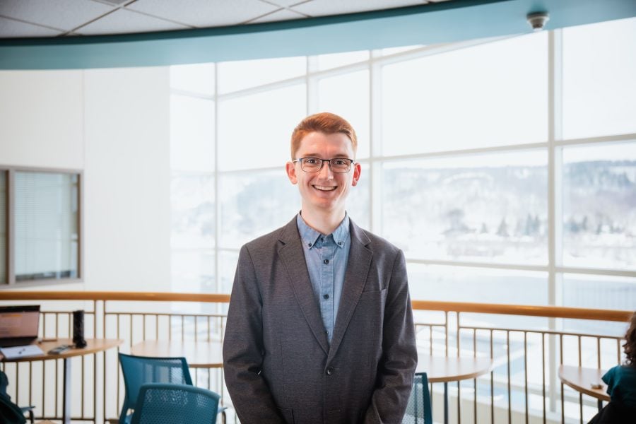 Undergraduate commencement speaker Caelan Mead-O’Brien stands in front of a sunny window in the DOW atrium. He is wearing a jacket and button-up shirt.
