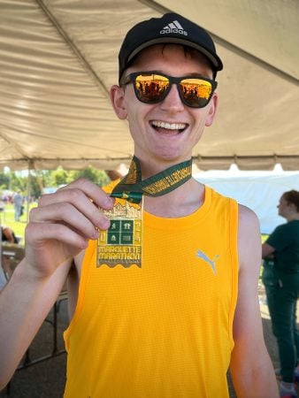 Caelan Mead-O’Brien poses with a green and yellow medal after completing a race in Marquette.