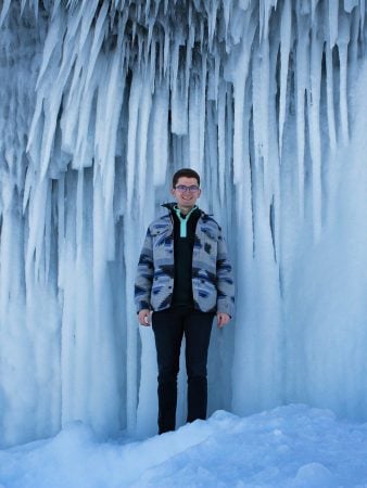 Undergraduate student speaker Caelan Mead-O’Brien stands underneath an ice formation at Presque Isle State Park.