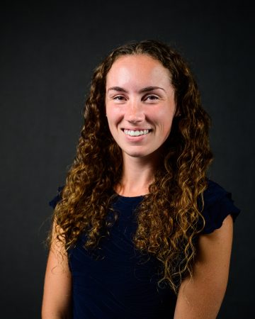Portrait of Madelyn MacRobbie wearing a blue shirt in front of the dark gray background.