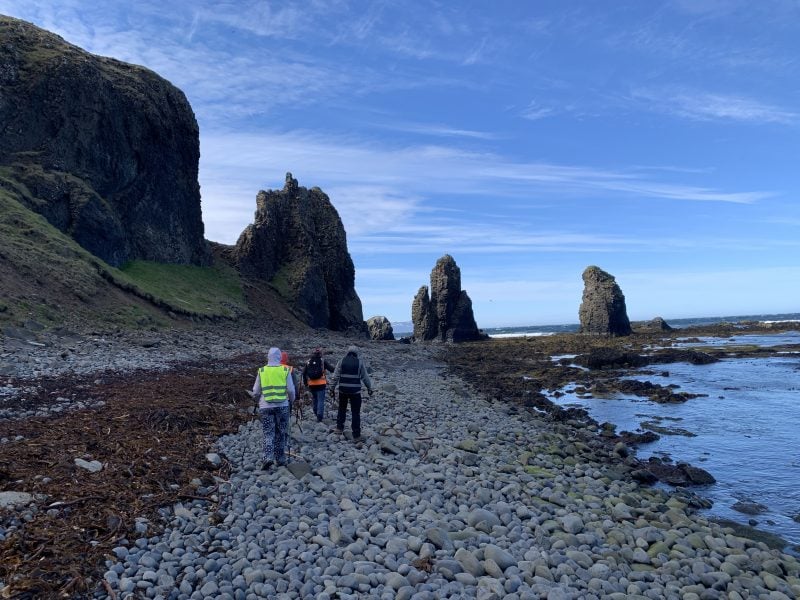 Researchers in reflective gear walk along a rocky shore in Iceland. 