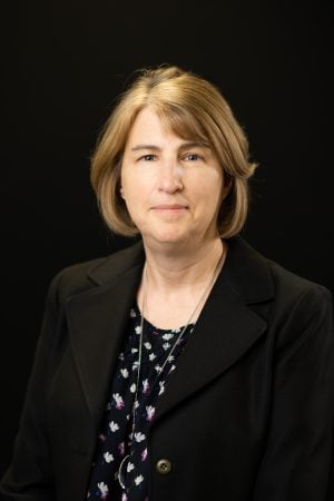 Headshot of Linda Wanless wearing a black blazer and floral blouse in front of a black background.