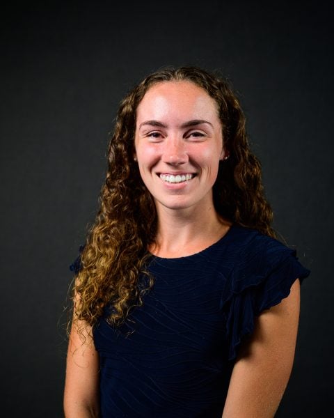 Headshot of Madelyn MacRobbie wearing blue in front of a dark gray background.