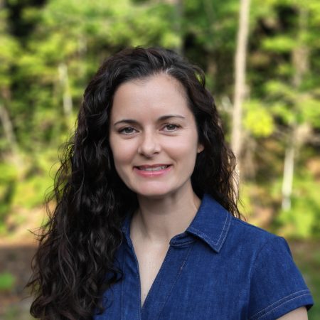 Headshot of Tracie Conn wearing a denim shirt in front of a plant background