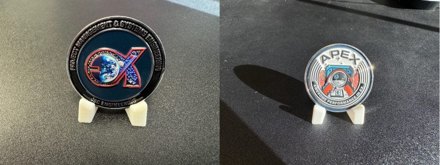 Two commemorative coins on display stands. The left coin reads 'Project Management and Systems Engineering, JSC Engineering' and features an EX logo. The right coin reads 'APEX – Awesome Performance in EX' and features an astronaut logo.