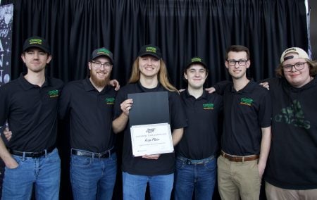 six students in black polos standing in front of a black curtain holding a first place certificate