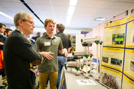 a student explains his research poster to a person judging