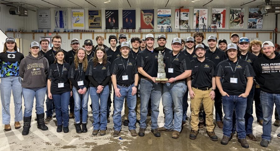 group photo of students wearing black polos and jeans standing in a line with the center two people holding a trophy