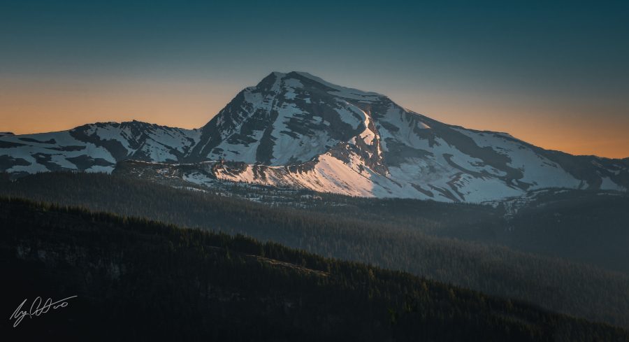 A mountain at sunrise overlooking miles of coniferous forests