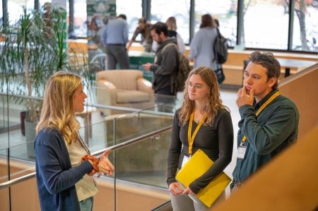 Three students stand talking on the atrium steps inside the Noblet Forestry Building.