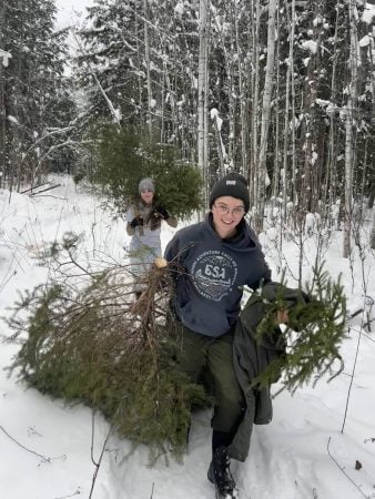  Two forestry club members carry evergreen trees through the snowy woods.