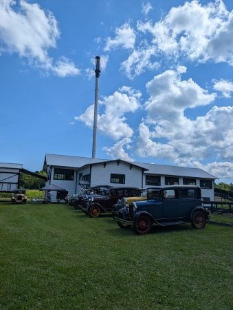Several classic cars sit parked on the lawn of the Ford Center near the sawmill.