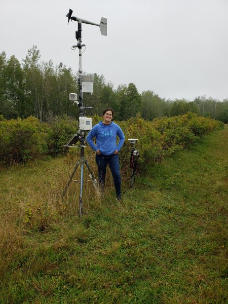Student standing in the field with two apparatuses.