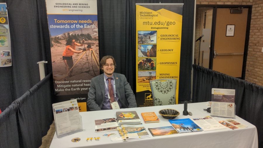 John sits at a table with brochures and MTU Geo Mining banners 