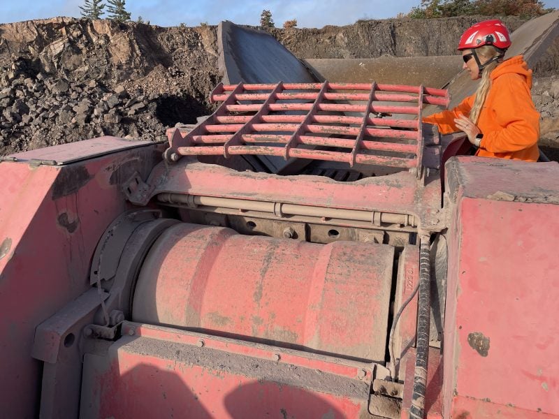 Young woman wearing safety gear operates large red industrial machinery outside with dirt behind